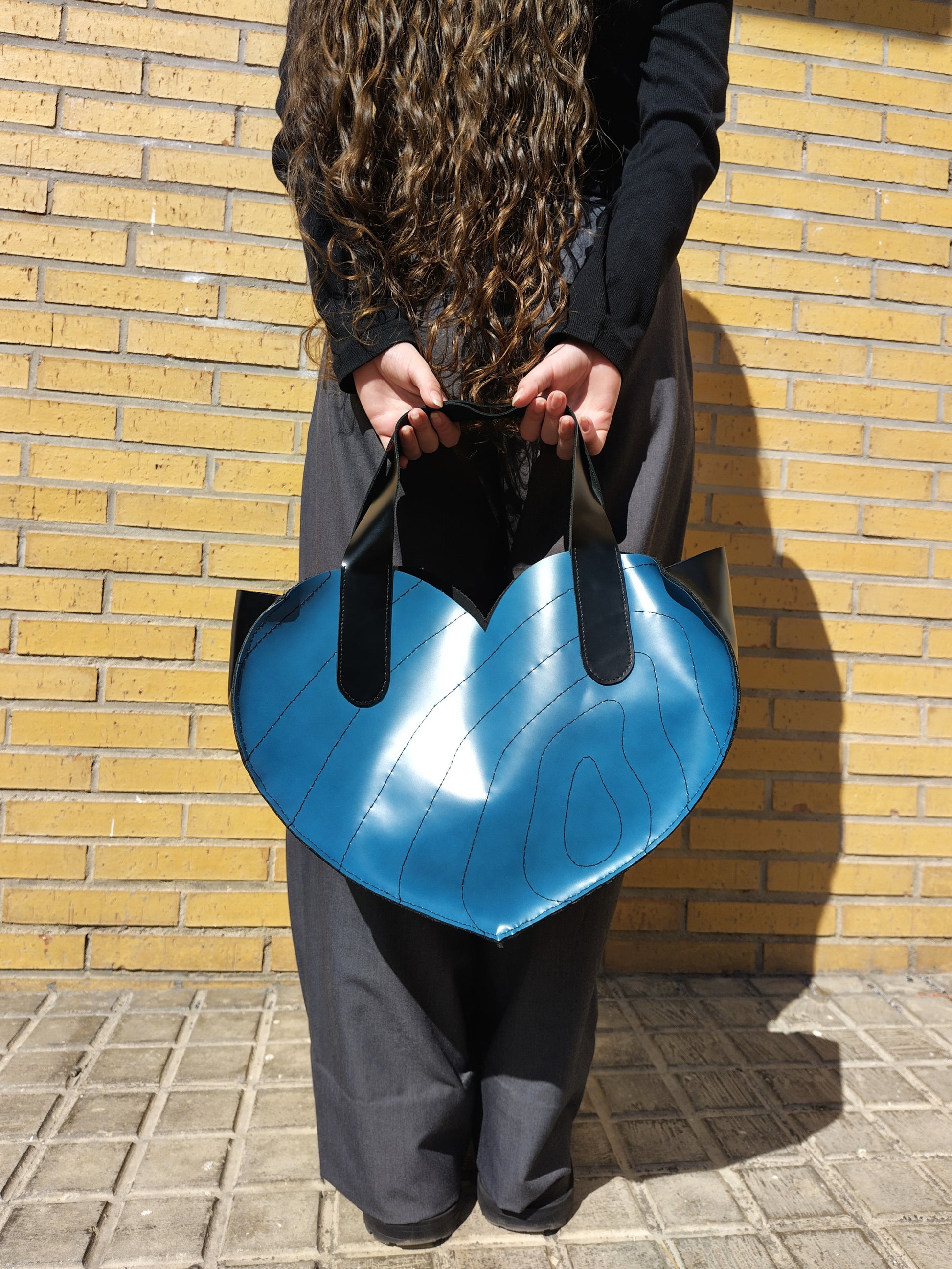 Bolso de cuero de asas grande en forma de corazón. Con frente azul bordado con líneas curvas nagras y laterales negros.
