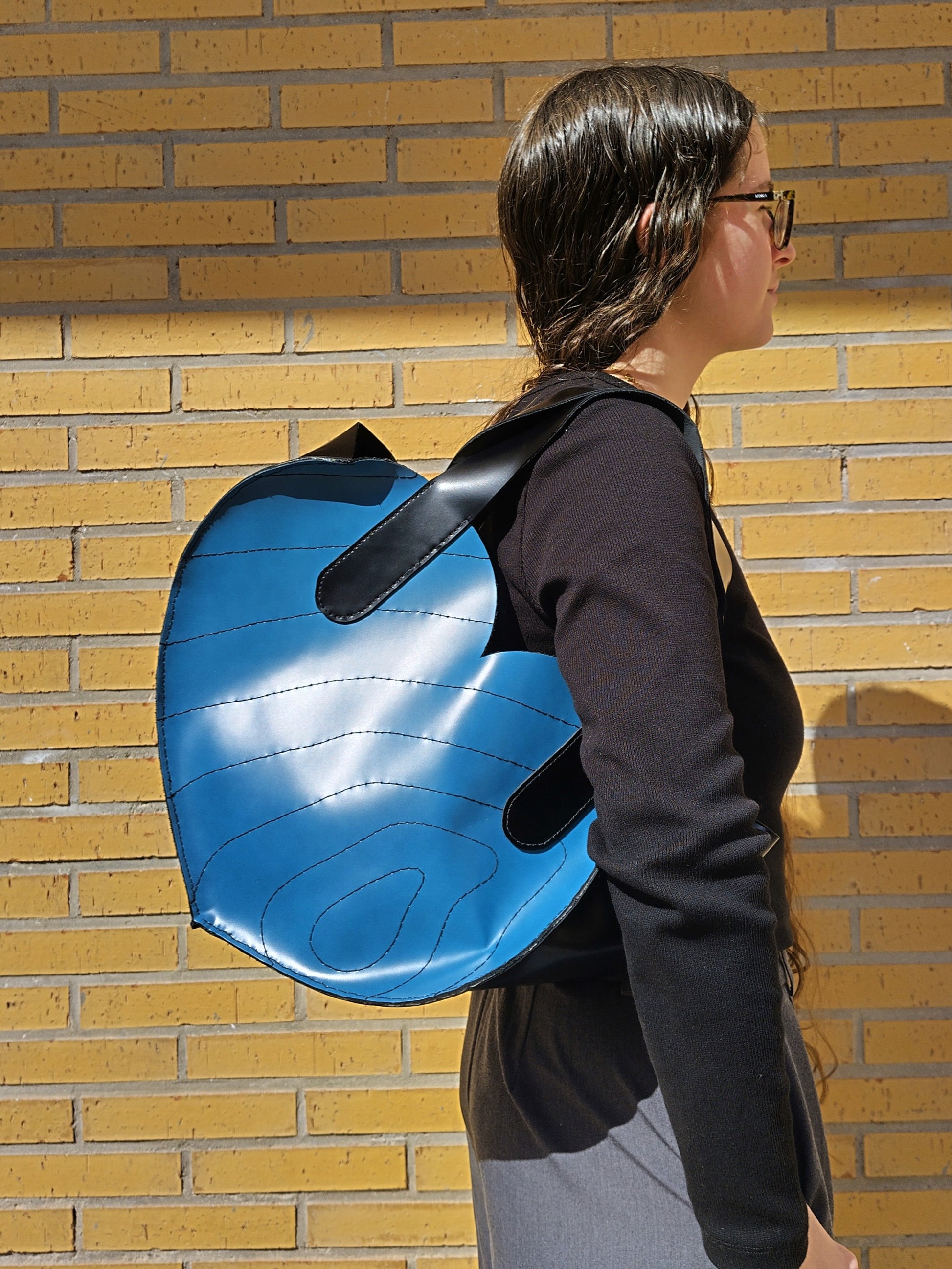 Bolso de cuero de asas grande en forma de corazón. Con frente azul bordado con líneas curvas nagras y laterales negros.