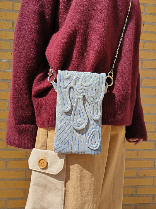 Bolso rectangular colgable, de tejido vaquero con cierre en forma de gotas cayendo. Con cadena desmontable de metal plateada.