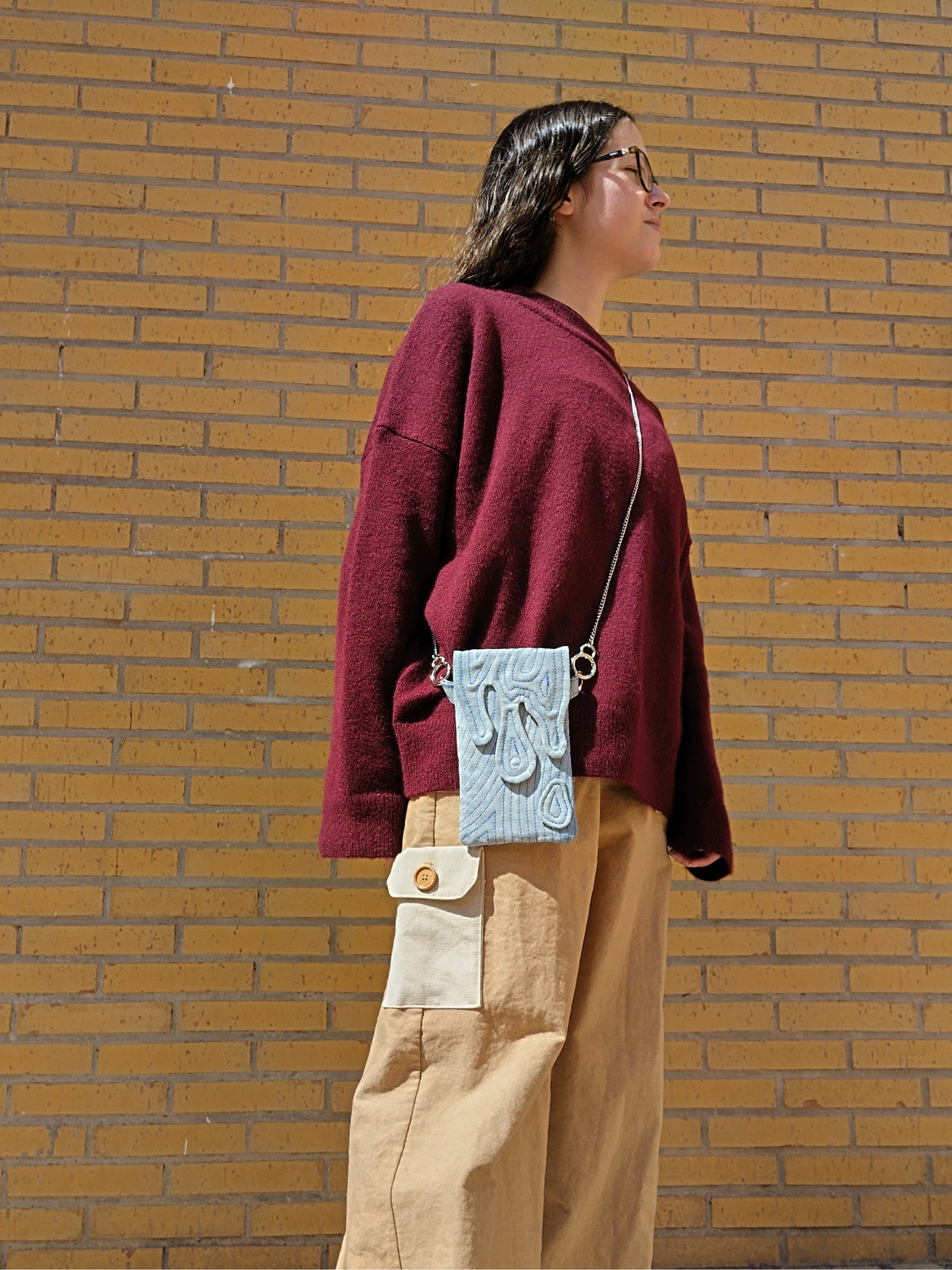 Bolso rectangular colgable, de tejido vaquero con cierre en forma de gotas cayendo. Con cadena desmontable de metal plateada.