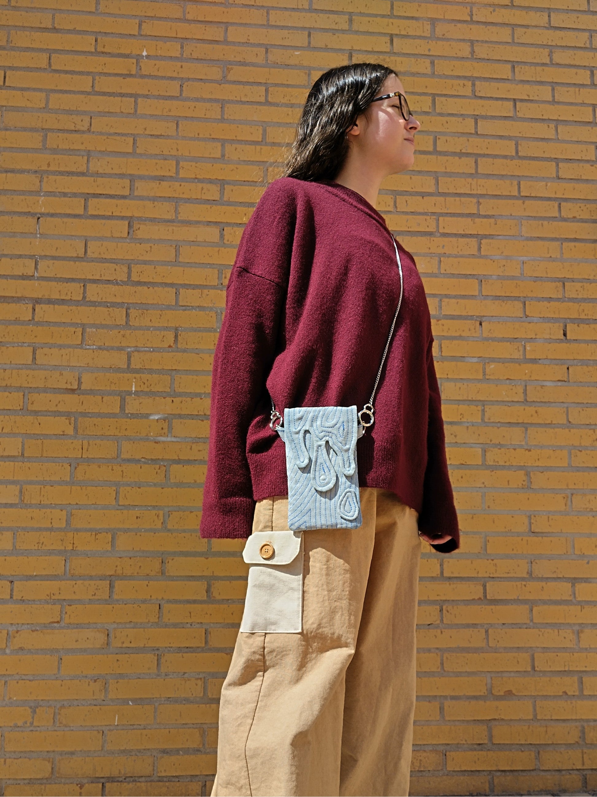 Bolso rectangular colgable, de tejido vaquero con cierre en forma de gotas cayendo. Con cadena desmontable de metal plateada.