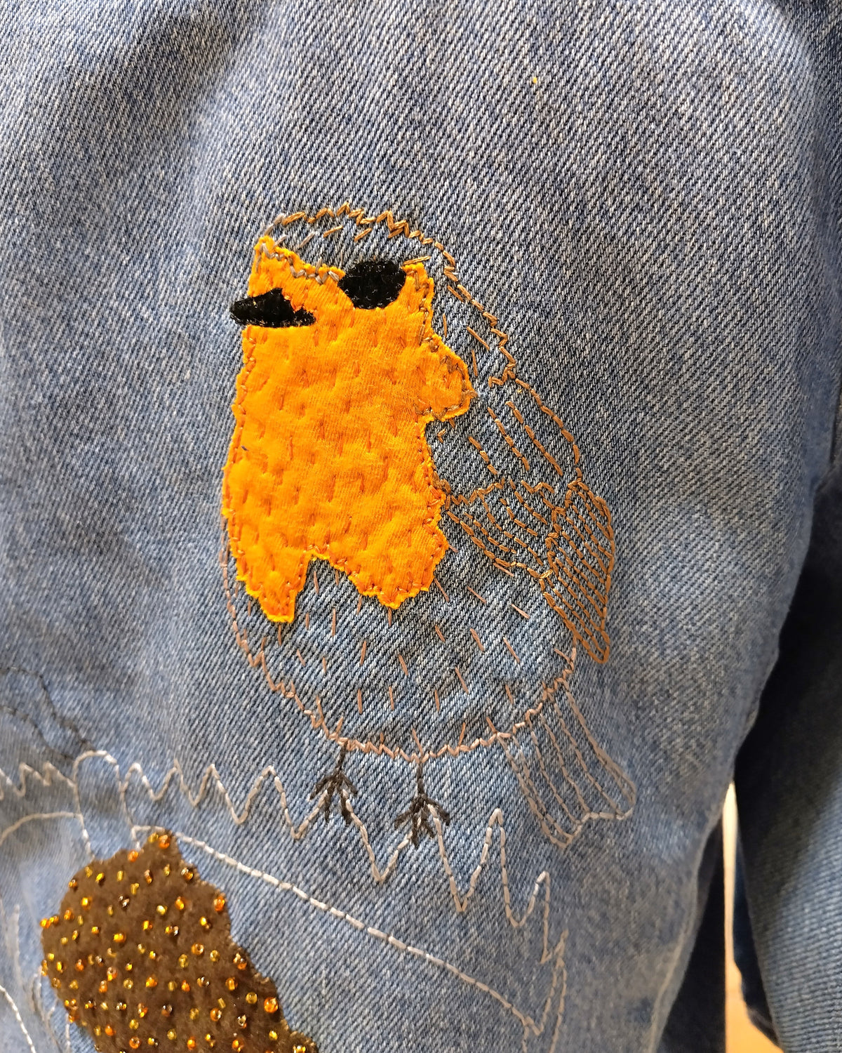 Detalle de bordado de un petirrojo en una chaqueta vaquera personalizada.