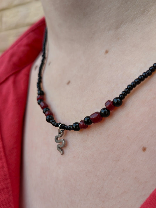Collar de cuentas de vidrio y piedra en negro y granate con colgante plateado de serpiente.