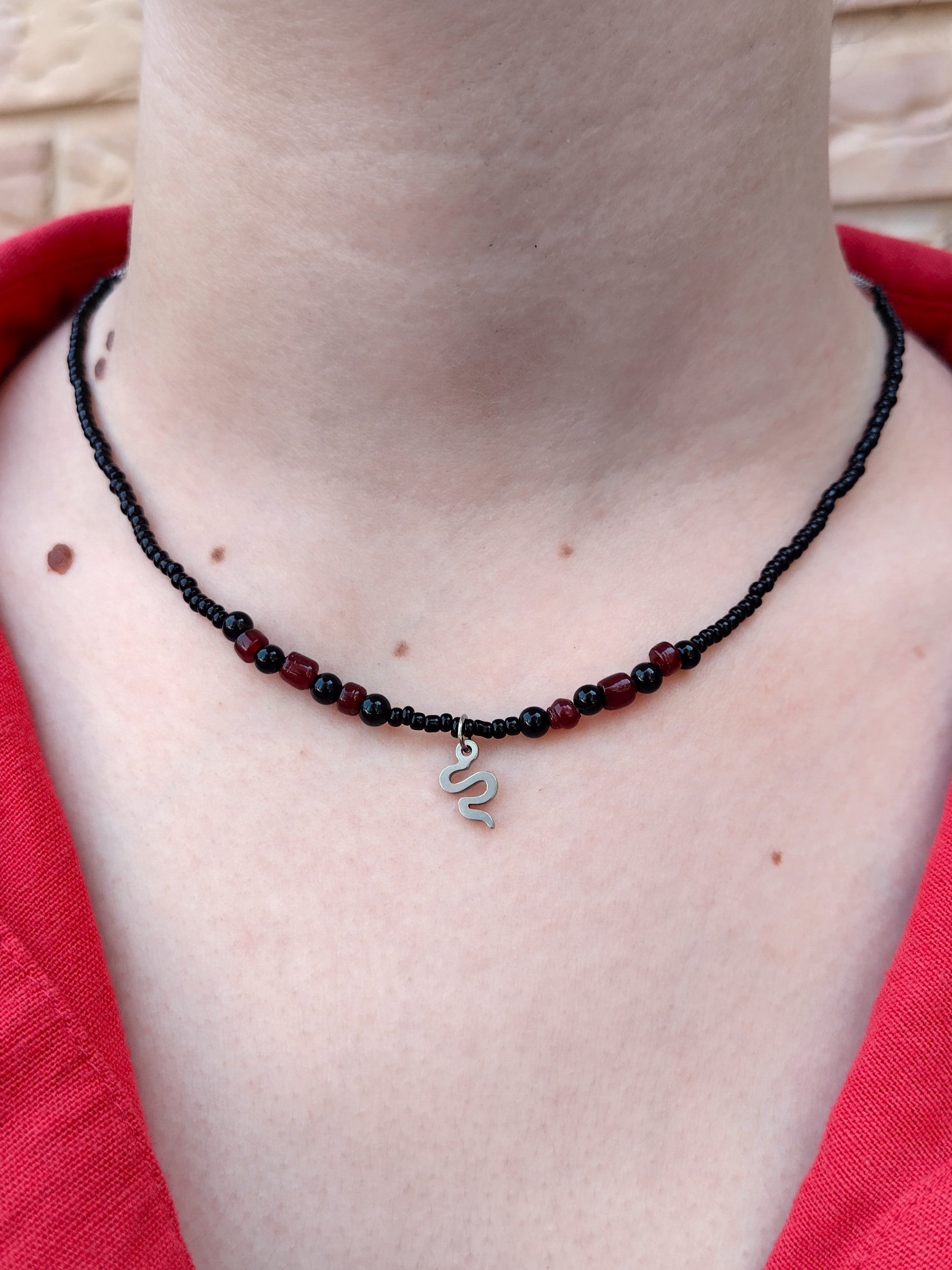 Collar de cuentas de vidrio y piedra en negro y granate con colgante plateado de serpiente.