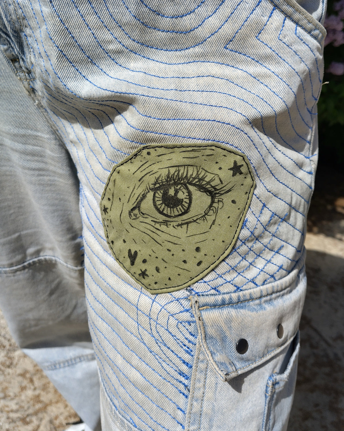 Detalle de personalización para un pantalón, es un parche verde pintado a mano alzada con el motivo de un ojo.